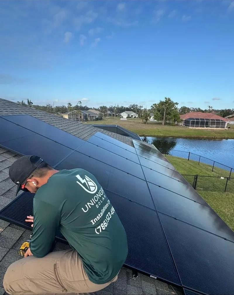 UnionGrid installer kneeling on a shingle roof mounting solar panels beside a canal-front home